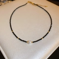 Collana minimalista con perline nere, perla bianca e accenti dorati su sfondo beige - Nero