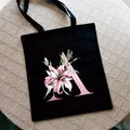 Bolso tote de lona negra con estampado de lirio rosa y letra A sobre estera tejida - Letra A / Negro