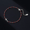 Detailed macro view of stainless steel cross bracelet with small red beads and lobster clasp - Silver-Red