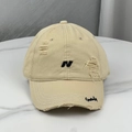 Close-up of distressed beige baseball cap with black letter N embroidery and torn brim detail - Khaki