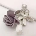 Macro detail of purple fabric rose, white tassel, and rhinestone enamel flower keychain - Gray