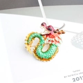 Broche de dragón chino esmaltado en rojo y verde con borde dorado sobre una revista - verde oliva