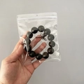 Hand holding a transparent PVC seal bag containing a black beaded jewelry bracelet - 25 Micron 12x15cm Perforated Resealable / 100 Pcs/Pack