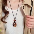 Close-up of amber resin teardrop pendant with black wax cord on a trench coat - 62# Necklace-Dark Brown