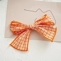Close-up of orange and white plaid fabric bow hair clip on a minimalist white background - Orange