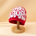 Red knit beanie with white jacquard letter pattern on a wooden stand in studio lighting - M (56-58cm) / Red & White