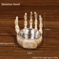 Skull hand resin holder with silver metal bowl on rustic wooden background - Skeleton Palm