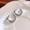Detailansicht der silbernen Knotenohrringe in C-Form auf einem Dekoteller aus Keramik - Silber