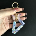 Detail of a resin alphabet V keychain with heart sequins, purple tassel, and butterfly charm - Letter V / Butterfly Tassel 8-Shape Buckle
