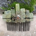 Macro detail of natural green crystal hair comb with silver sun totem on mossy background - Prehnite Black Wire Silver Sun