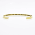 Macro view of golden stainless steel cuff with engraved motivational quote on inner band - BEAUTIFUL GIRL, YOU CAN DO HARD THINGS