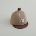 Dettaglio di un cappello morbido per neonati con lettera M e visiera a contrasto - 48cm (Neonato) / Caffè Cachi