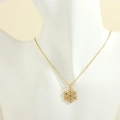 Close-up of golden snowflake pendant necklace with green gemstone on a display stand - Snowflake