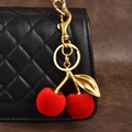 Charm de sac cerise rouge velouté avec détails en métal doré sur un sac à main noir - Cerise Rouge Flocage