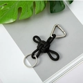 Llavero de cuerda de nailon trenzado negro con hebilla triangular plateada sobre revista - Negro