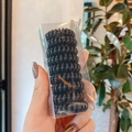 Hand holding a container of high-elasticity black spiral telephone cord hair ties - 18# Medium Black