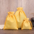 Three bright yellow drawstring linen pouches in different sizes on wooden texture background - Bright Yellow