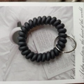 Matte black spiral coil wrist keychain with a silver metal ring on decorative paper - Black