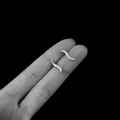 Macro shot of minimalist silver S-shaped stud earrings held on finger for scale - 925 Silver / Silver