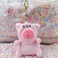 Cute pink plush pig keychain with golden metal hook and colorful foam bead background - Pig Hat Pink + Gold Clip