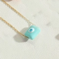 Macro view of a gold chain with a rectangular light blue evil eye pendant on a white background - Blue
