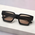Detail view of thick black square sunglasses with light brown lenses on a display stand - Black Frame Tea Lens