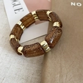 Detailaufnahme von bernsteinfarbenem Harz-Bambusarmband mit goldmetallischen Akzenten - Dunkelbraun