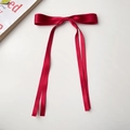 Detail view of a red satin ribbon bow hair clip with long streamers on a white surface - Red