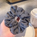 Chouchou en laine grise avec nœuds brodés noirs présenté dans un café cosy - Broderie Nœud / Gris