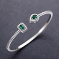 Detailed close-up of silver open bangle with pear and emerald cut green stones - Silver + Green Zirconia