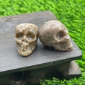 Set of two hand-carved natural beige crystal skull figurines on a dark wood base - Indian Red Jade