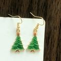 Detail shot of green Christmas tree earrings with gold finish and red dots on wooden surface - Simple Green Enamel Tree