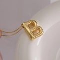 Gold balloon letter B pendant necklace with polished finish on a white ceramic display - Letter B