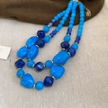 Detail of layered blue acrylic chunky beads and gold spacers on a rustic fabric background - Blue