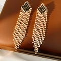 Primer plano de pendientes vintage con borlas de diamantes blancos sobre cuero marrón - Pin de plata - Dorado - Negro