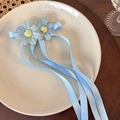 Detail van een lichtblauwe bloemen haarspeld met zijden linten op een keramisch bord - Blauwe Strik