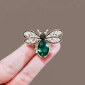 Golden bee brooch with emerald gemstone and sparkling crystals held by fingers - Style 24