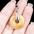 Polished round yellow jade donut pendant with silver clasp held by hand - 20mm Yellow Topaz Jade