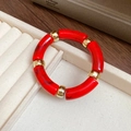 Red marble acrylic tube bracelet with gold metal spacers on a white velvet display - Red