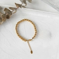 Drielaagse 18K vergulde kralenarmband met K18-label op een witte getextureerde basis - Gouden Armband