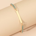 Gold chain bracelet with blue crystals and a flat rectangular metal tag on beige display - KC Gold Blue Rhinestone Square Plate Style (9525)