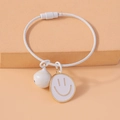 Dettaglio di un bracciale in filo bianco con pendente smiley e perla su fondo beige - Bianco
