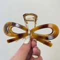 Gros plan d'une pince à cheveux en acétate écaille de tortue avec design de nœud doré - Pince 11.5cm / Ambre