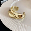 Vista detallada de un brazalete abierto dorado ondulado sobre un plato blanco texturizado - Dorado - Ancho Irregular