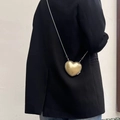 Detailaufnahme einer goldenen herzförmigen Umhängetasche mit glänzendem Finish und Kette. - Gold