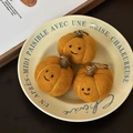 Three handmade orange wool felt pumpkin keychains with smiling faces on a vintage plate - Autumn Pumpkin Trio