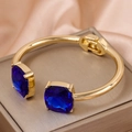 Luxurious gold-tone open bangle with two large square blue crystals on a silk background - Gold Square Blue Zirconia