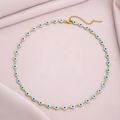 Close-up of golden chain necklace featuring blue evil eye beads on pink fabric - White and Blue