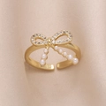 Bague nœud dorée élégante avec zircons et perles sur fond en soie luxueux - Style D-Nœud Papillon Pompon De Perles Avec Zircone