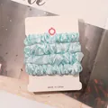 Detail view of light blue satin scrunchies set on professional white display card - Sky Blue